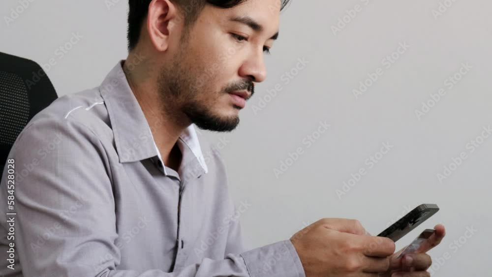 Handsome Asian man entering his credit card number into his mobile phone to pay for a service or shopping online. Handsome Asian man entering his credit card number into his mobile phone to pay for a service or shopping online.