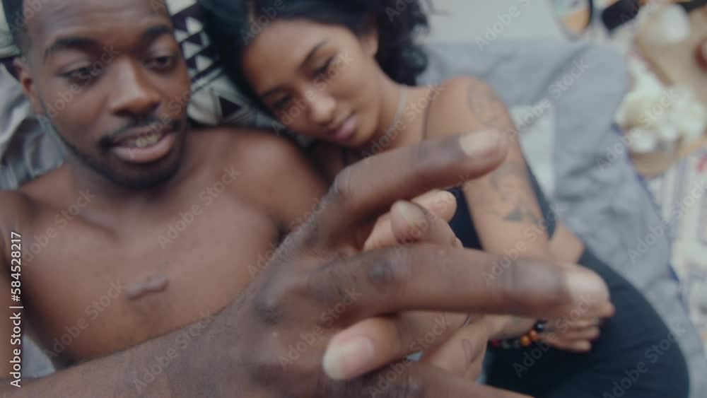 Young affectionate couple lying down on bed, smiling, touching hands gently, enjoying romantic time together at home. Top down shot, racking focus Young affectionate couple lying down on bed, smiling, touching hands gently, enjoying romantic time together at home. Top down shot, racking focus