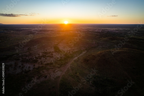 Looking down at a remote mountainous landscape as the sun rises over the horizon