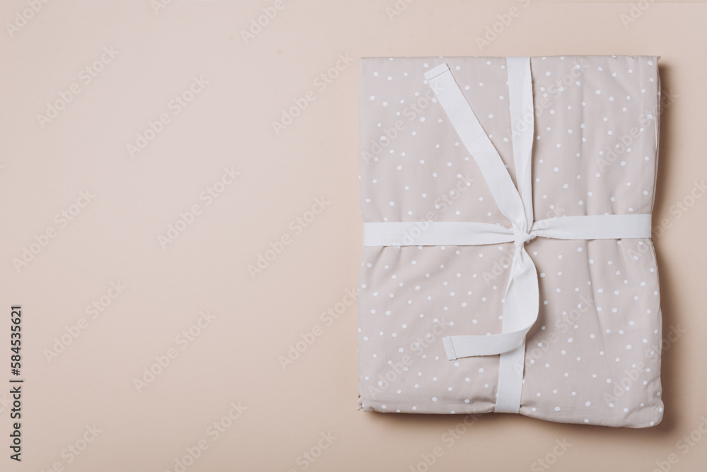 Stack of clean bed sheets with bow for present or gift on beige background. Top view. Copy space Stack of clean bed sheets with bow for present or gift on beige background. Top view. Copy space