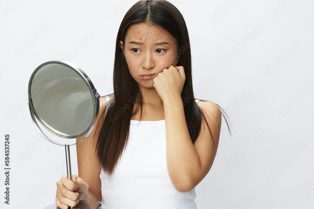 Asian woman with mirror in hand facial skin problems, acne and inflammation, red rash and allergies, chicken pox, sadness from rashes. Facial skin care concept for diseases and nerves Asian woman with mirror in hand facial skin problems, acne and inflammation, red rash and allergies, chicken pox, sadness from rashes. Facial skin care concept for diseases and nerves