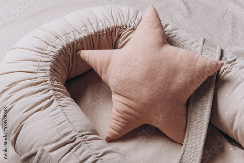 Soft star pillow toy on beige cocoon, baby nest for newborn over cribs in nursery. Childhood concept. Eco-friendly safe goods and toys for children. Light kid's room interior. Time for sleep