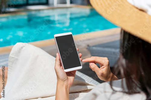 Wallpaper Mural Asian woman sitting on sunbed near swimming pool using mobile phone. Young traveler girl working on cell phone during her summer holiday. Technology and lifestyle concept. Free space Torontodigital.ca