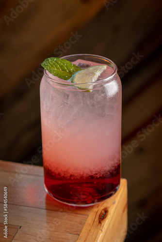 Fresh Strawberry Italian Soda topped with cut strawberry and rosemary leaves in a drinking glass with white straw.