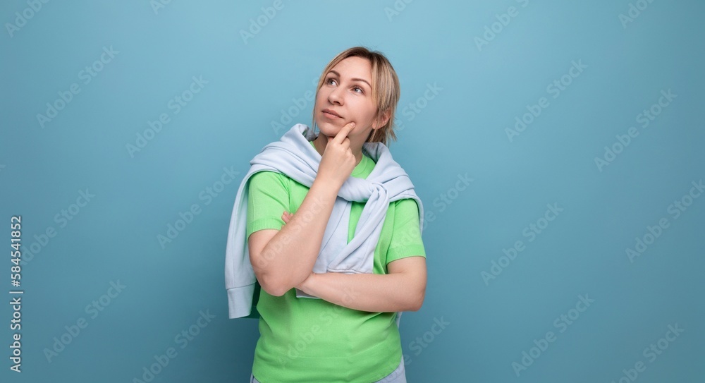 portrait of a blond cute young woman in a casual outfit looks thoughtfully to the side on a studio blue background with copy space portrait of a blond cute young woman in a casual outfit looks thoughtfully to the side on a studio blue background with copy space
