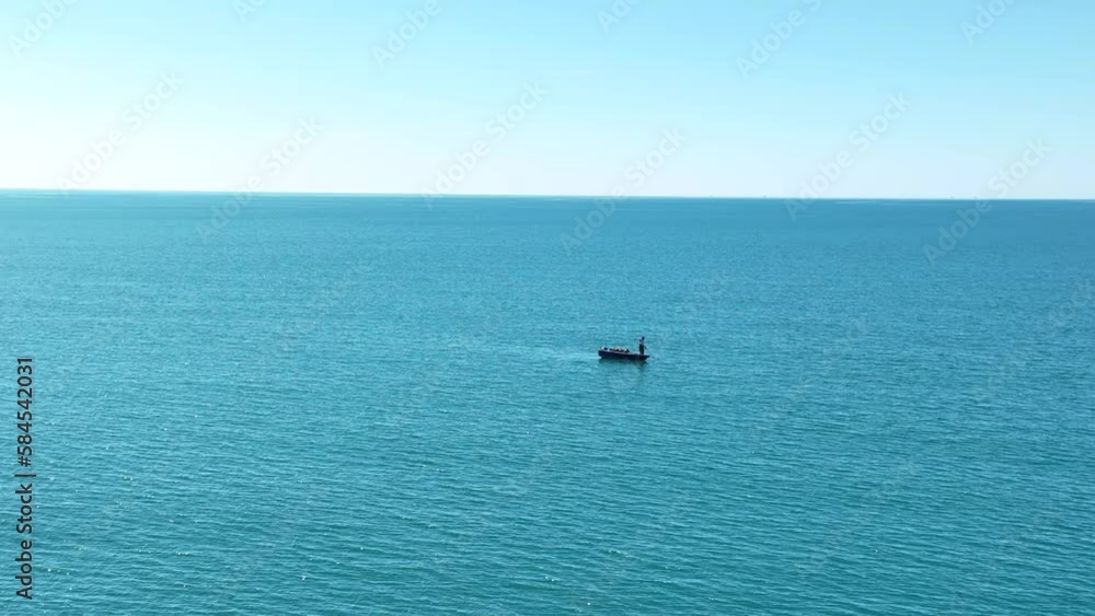 Aerial static shot of lone man standing on small boat in open seas Aerial static shot of lone man standing on small boat in open seas