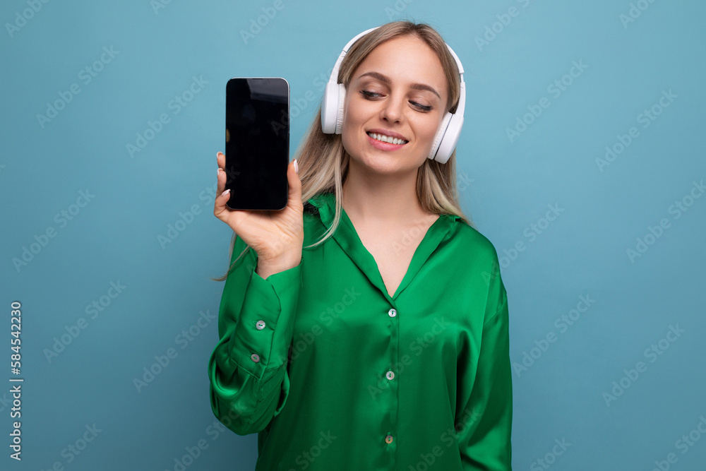 photo of stylish european girl showing smartphone screen with mocup on blue studio background with free space photo of stylish european girl showing smartphone screen with mocup on blue studio background with free space