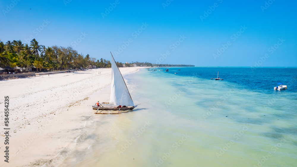Obraz premium Take in the breathtaking beauty of Zanzibar's tropical coastline from above, as fishing boats dot the sandy beach at sunrise. The view from the top highlights a clear blue sea, green palm trees,