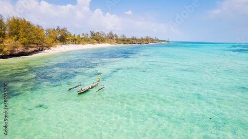 Take in the breathtaking beauty of Zanzibar's tropical coastline from above, as fishing boats dot the sandy beach at sunrise. The view from the top highlights a clear blue sea, green palm trees, 