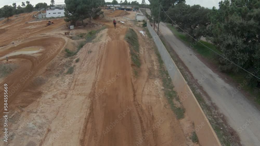 Wide aerial FPV slow motion follow of motocross rider jumping high, sky reflect in mud Wide aerial FPV slow motion follow of motocross rider jumping high, sky reflect in mud