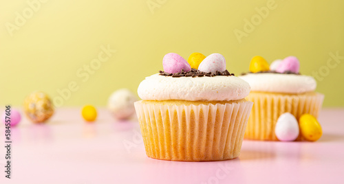 Easter cupcake decorated with cream, chocolate sprinkles, sweet eggs close-up. Blurred background banner in pink and yellow.
