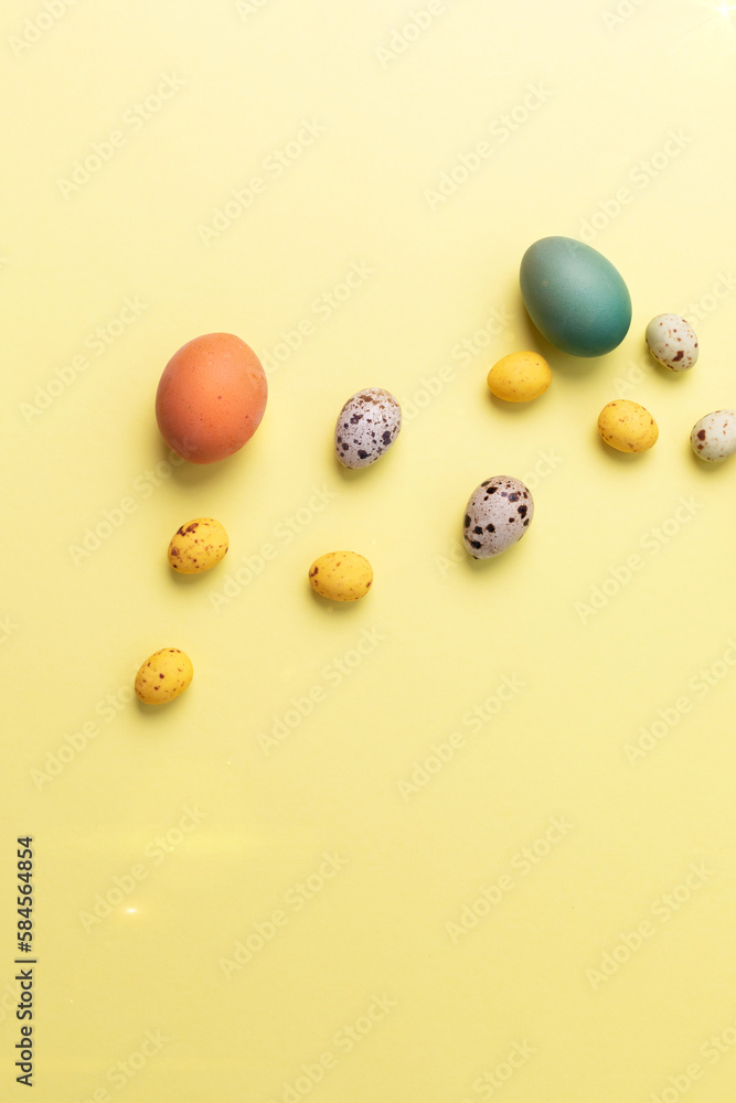 Colored eggs of different sizes on a yellow background. Symbol of the Easter holiday. Easter background. Flat lay