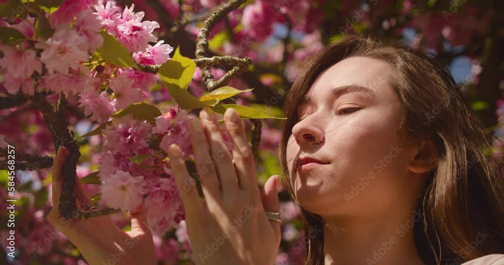 Pretty woman smelling and touching blooming cherry blossom in garden during spring season