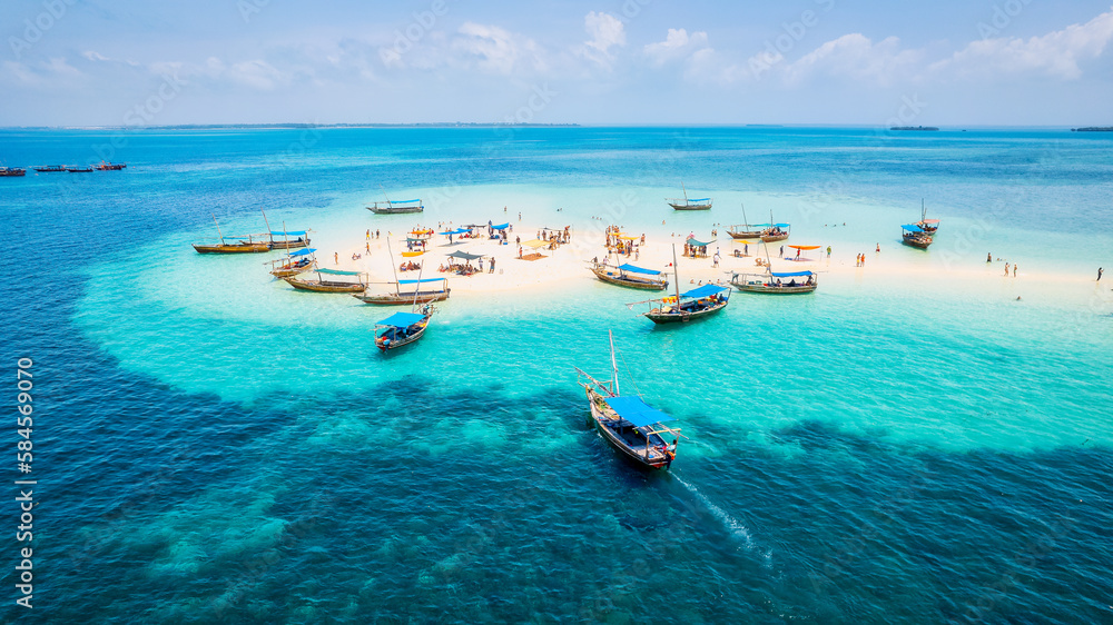 The natural beauty of Zanzibar's tropical coast is on full display in this aerial view, with fishing boats lining the sandy beach at sunrise. The top-down perspective showcases clear blue waters,