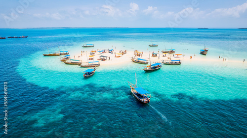 The natural beauty of Zanzibar's tropical coast is on full display in this aerial view, with fishing boats lining the sandy beach at sunrise. The top-down perspective showcases clear blue waters,