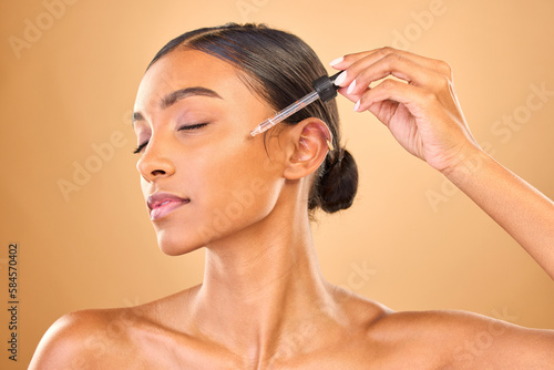 Face, skincare serum and woman with eyes closed in studio isolated on brown background. Dermatology, cosmetics and Indian female model with hyaluronic acid, retinol or essential oil for healthy skin. photo