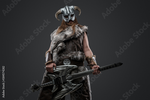 Portrait of scandinavian warrior with electric guitar and horned helmet looking at camera.