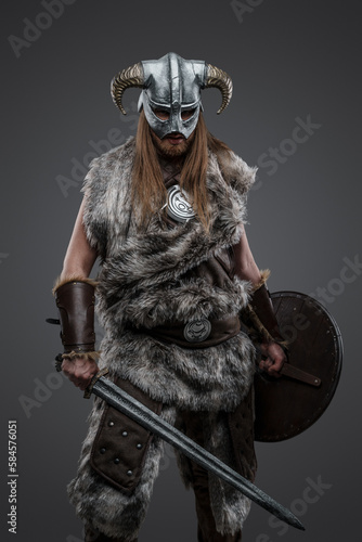 Shot of ancient viking dressed in fur and horned helmet against gray background.