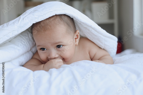 Cute baby boy crawling on the bed while playing with hands, body covered by the blanket. Happy moments.