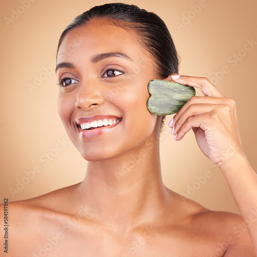 Beauty, gua sha and face of Indian woman for skincare, facial treatment and wellness with spa tools. Salon, dermatology and happy girl on brown background for cosmetics, face massage and luxury stone