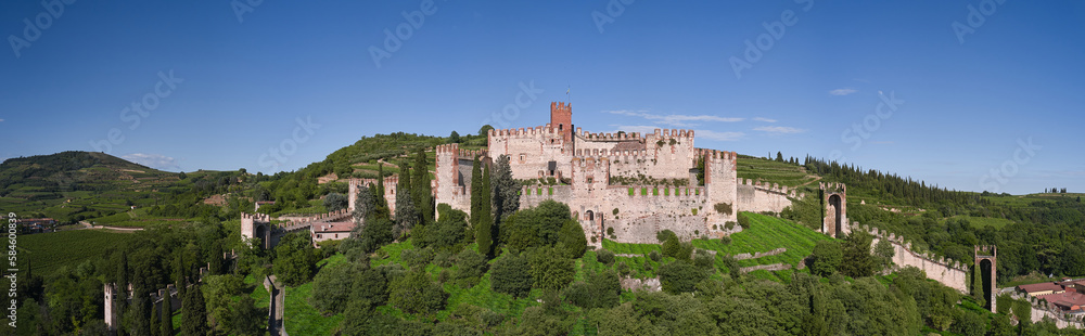 Panoramic view of Soave castle surrounded by vineyard plantations. Soave castle aerial view Verona province, Italy. Ancient castle on a hill in Italy. Italian flag on the main tower of Soave Castle.