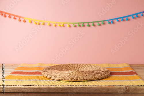 Empty wooden table with wicker place mat over pink wall  background. Mexican party mock up for design and product display