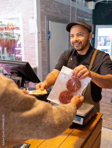 butcher at the butcher's shop charging cash for some hamburguers. Shopkeeper performing the action of charging for two hamburgers while handing them out photo