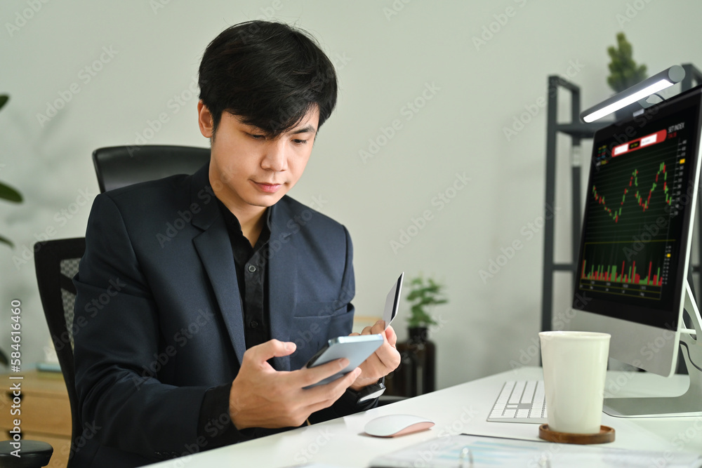 Handsome male financial analyst using mobile phone and monitoring stocks data candle charts on screen Handsome male financial analyst using mobile phone and monitoring stocks data candle charts on screen