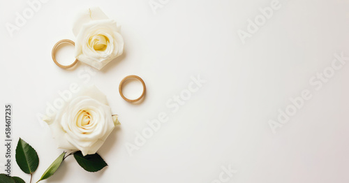 White beige background with white roses and gold wedding rings. Top view banner with plenty of copy space.