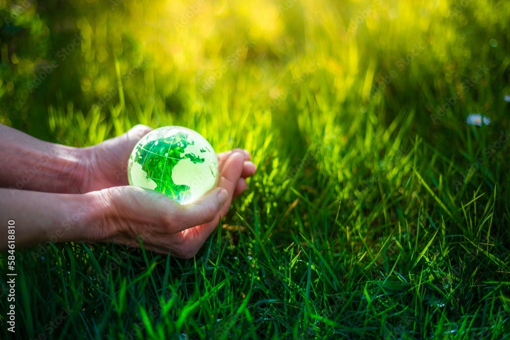 Hands holding glass Earth globe in green grass. Earth Day environment ...