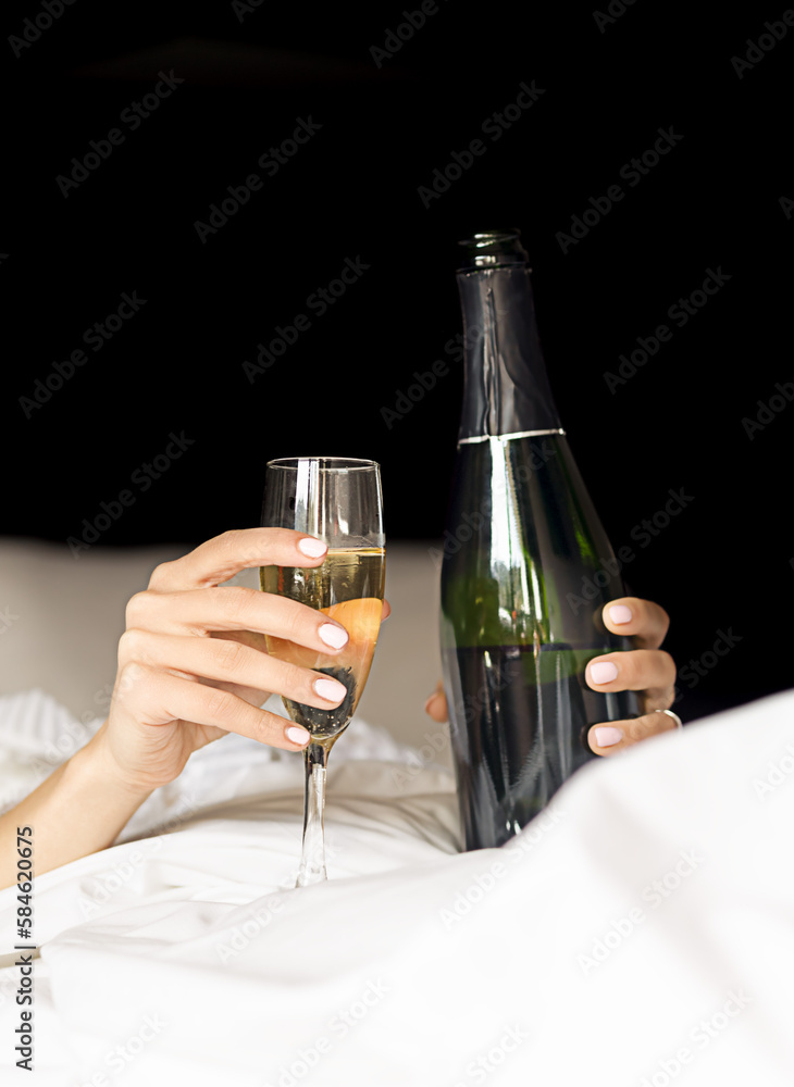 hands of a woman lying in bed with a glass and a bottle of champagne, celebrations and morning concept, hangover and bad after parties, hangover tips