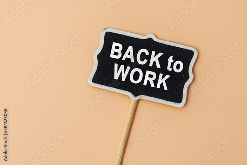 Back to work - text on a small chalkboard on a beige background. Top view. The concept education, training, after vacation, maternity leave, break