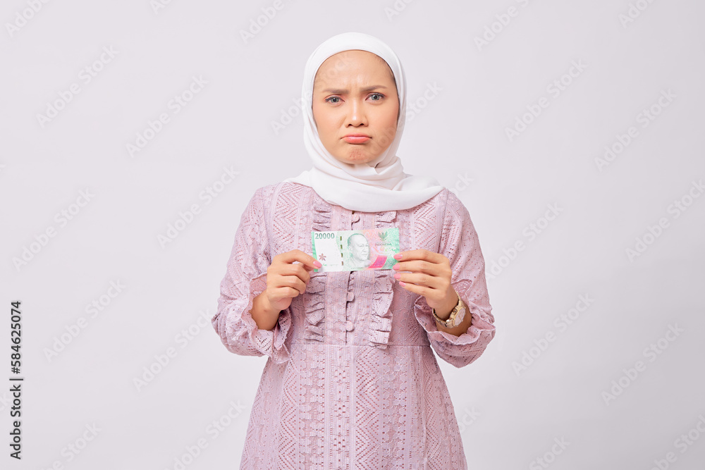 Pensive young Asian Muslim woman wearing hijab and purple dress holding fan of cash money isolated on white studio background Pensive young Asian Muslim woman wearing hijab and purple dress holding fan of cash money isolated on white studio background