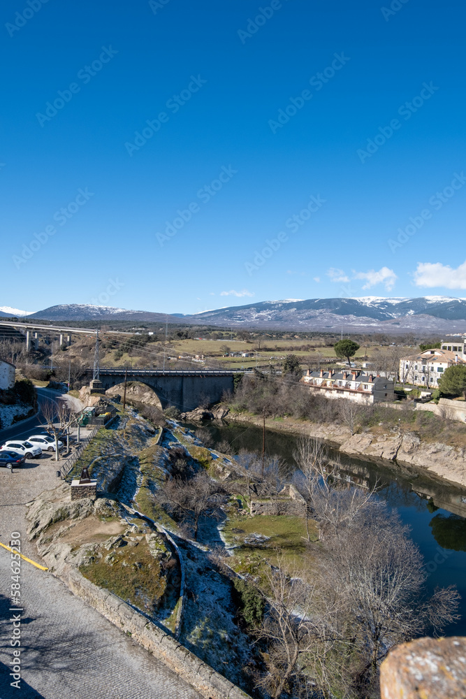 Panorámica del pueblo madrileño de Buitrago de Lozoya con el río rodeándolo bajo un cielo soleado.