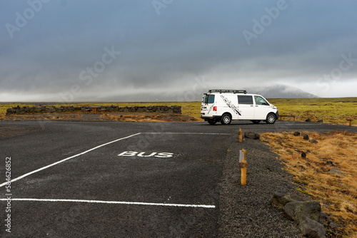 Van aménagé garé un bord d'un parking devant un arrêt de bus au milieu de la nature sauvage verte et jaune d'Islande 