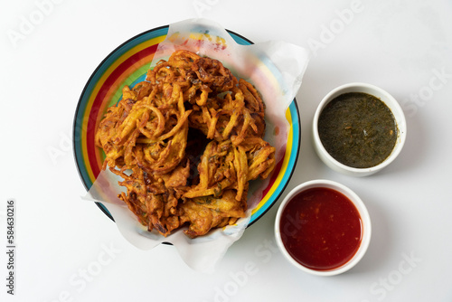 Fried onion pakora favourite Indian-pakistani Tea-Time snack during the rainy season. served with mint and sweet chilli sauces on textured background photo
