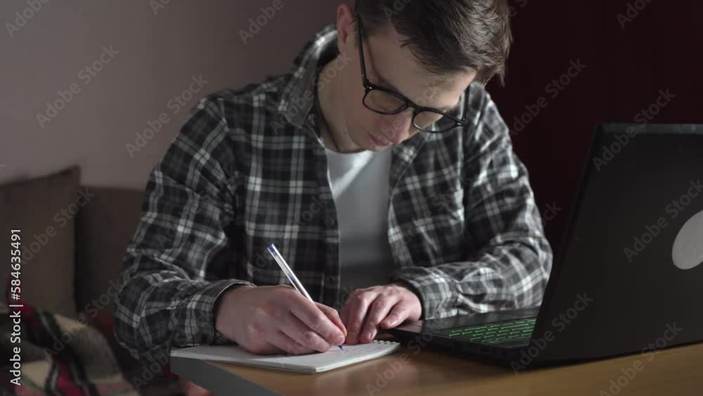 A young man notes an online lecture in a notebook. distance education. slide. A young man notes an online lecture in a notebook. distance education. slide.
