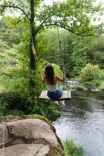 Girl on a swing over a river, inside a green forest in Galicia. Nature. Adventure.