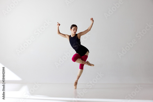 Adorable ballerina wearing pointe shoes dancing and looking away over white background