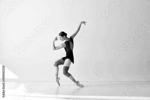 Monochrome. One emotional ballerina wearing pointe shoes dancing on fingertips with hands over white and black background