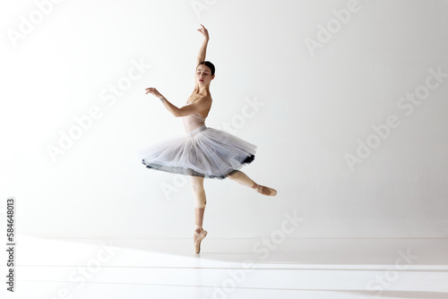 Portrait of tender young ballerina dancing, performing over white studio background. Beauty of classical dance
