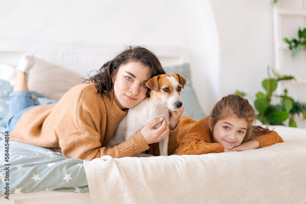 Happy mom and daughter play with their adorable wired Jack Russell Terrier puppy at home. Loving family with a puppy in the bedroom. Background, close-up, copy space. Happy mom and daughter play with their adorable wired Jack Russell Terrier puppy at home. Loving family with a puppy in the bedroom. Background, close-up, copy space.