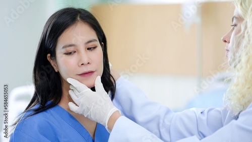 Asian woman patient face before cosmetic surgery and professional woman plastic surgeon wearing gloved hands inspecting at the clinic