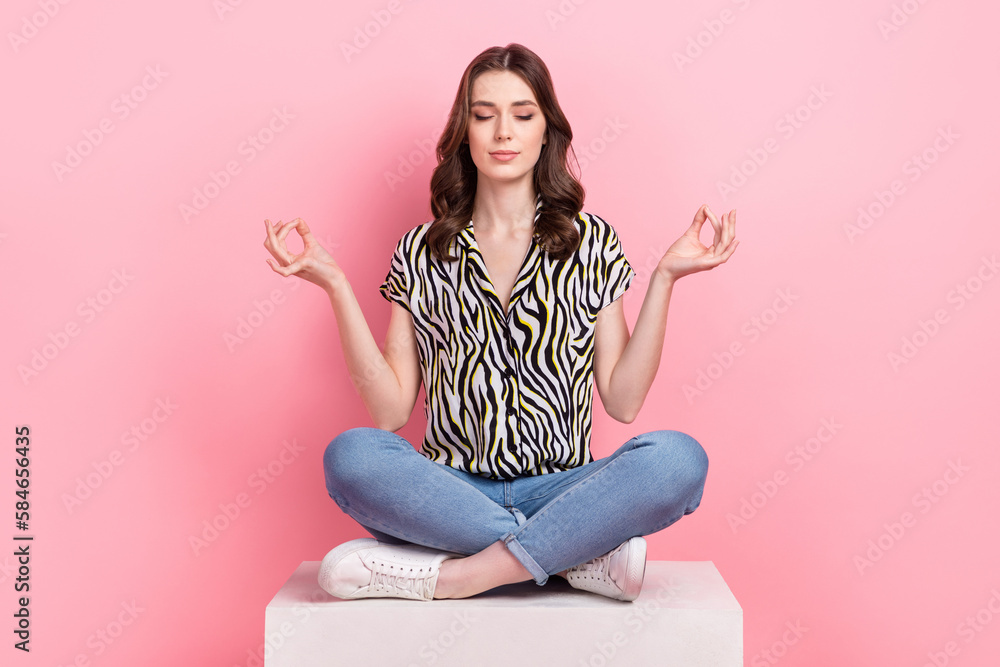 Full size photo of peaceful pretty girl sit podium crossed legs meditate isolated on pink color background Full size photo of peaceful pretty girl sit podium crossed legs meditate isolated on pink color background