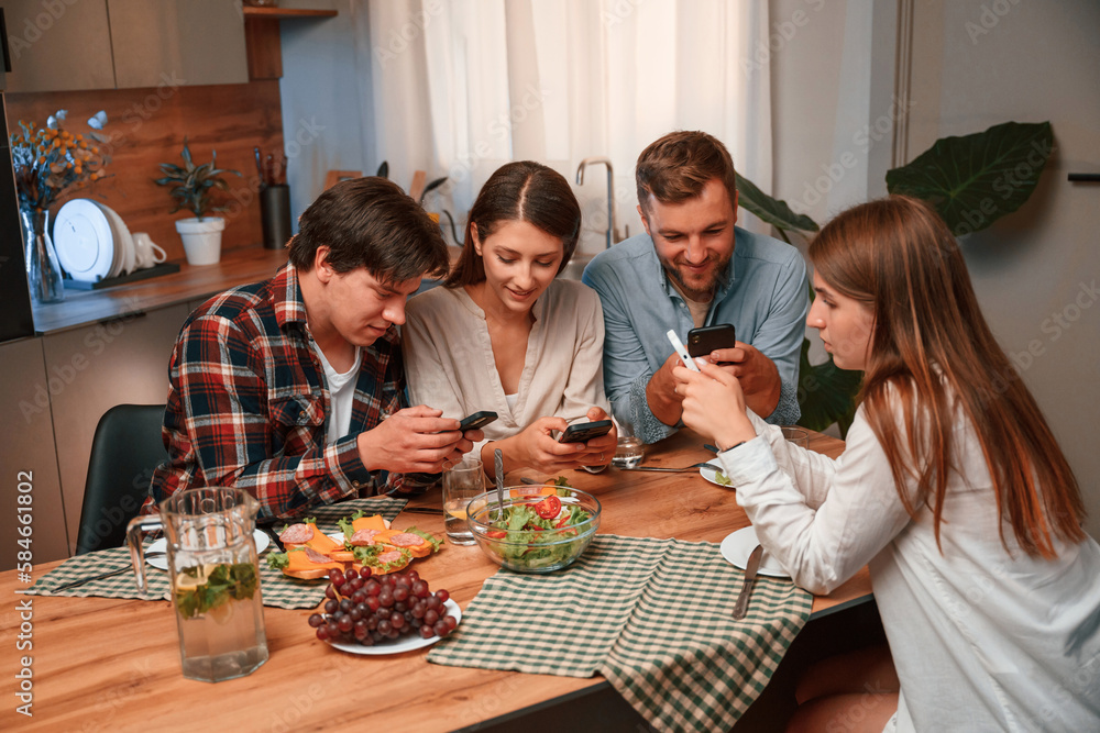 Using smartphone. Group of people are on the kitchen, having dinner, spending time together Using smartphone. Group of people are on the kitchen, having dinner, spending time together
