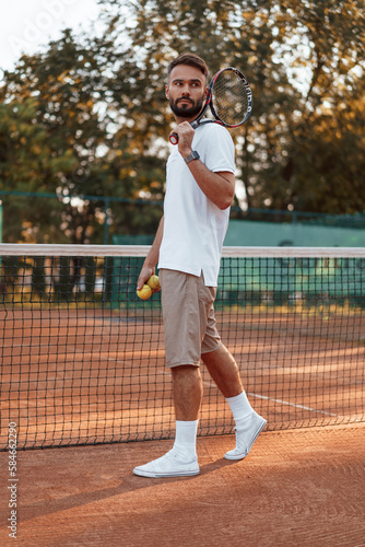 With racket and ball. Young man is on the tennis court at sunny daytime © standret