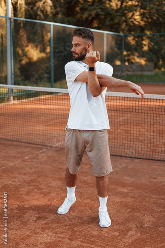 Warm up exercises. Young man is on the tennis court at sunny daytime
