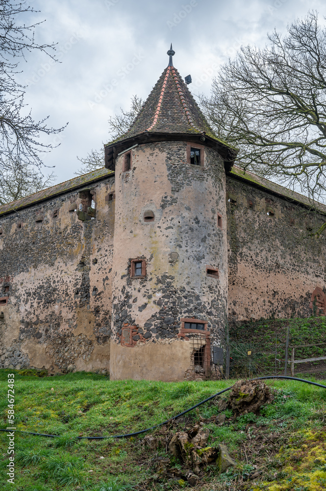 Old walls of Ronneburg Castle with a round tower and meadow in front during cloudy day, Germany, vertical shot