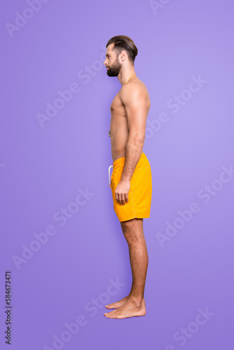 Side view snap full size fullbody portrait of attractive strong lifeguard with stubble, modern hairstyle in yellow shorts isolated on grey background