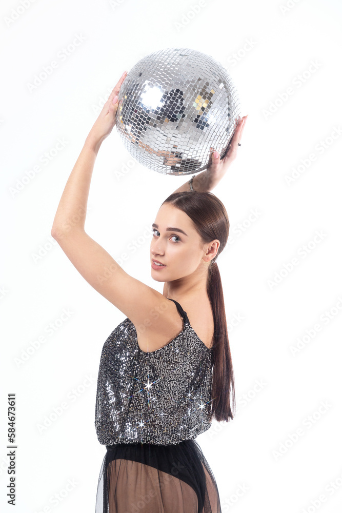 Naklejka premium A young woman in a black shiny bodysuit and a transparent tulle skirt poses with a disco ball on a white background.